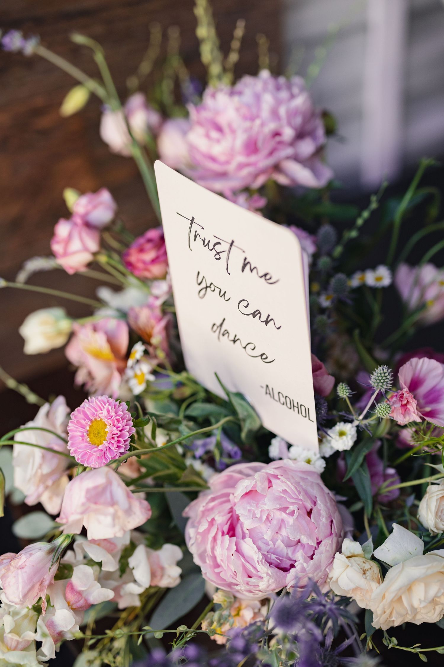 Handwritten note reading 'Trust me you can' placed among pink peonies and mixed pastel flowers in a floral arrangement.