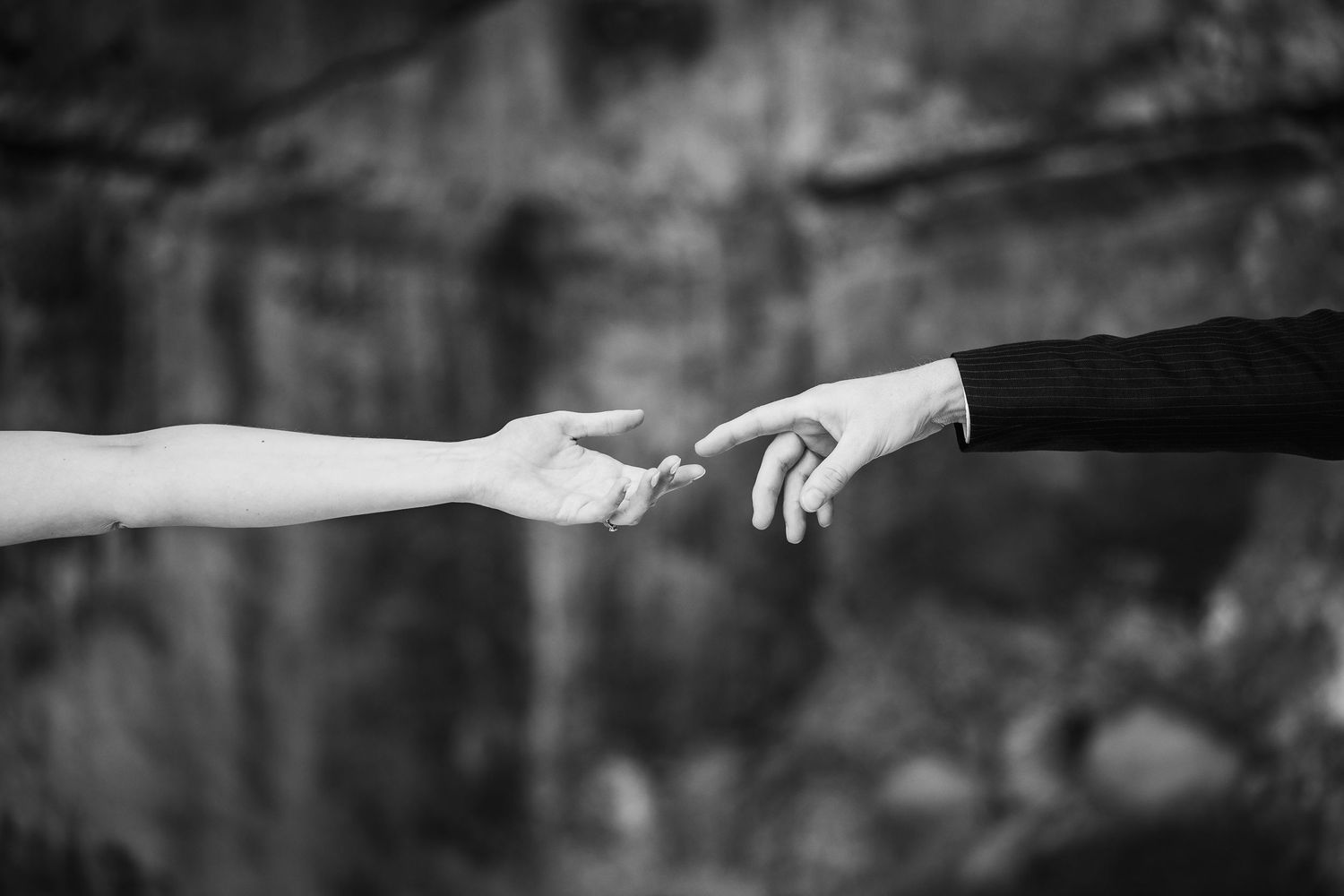 Two hands reaching towards each other against a blurred dark background in black and white photography.