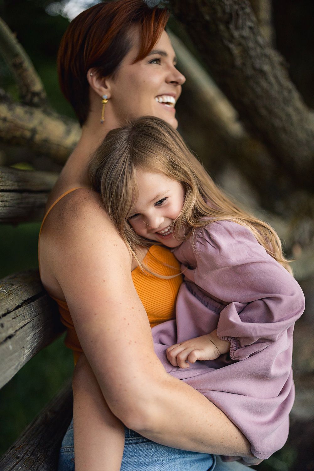 A tender moment shows a parent and child cuddling and laughing together on a wooden bench outdoors.