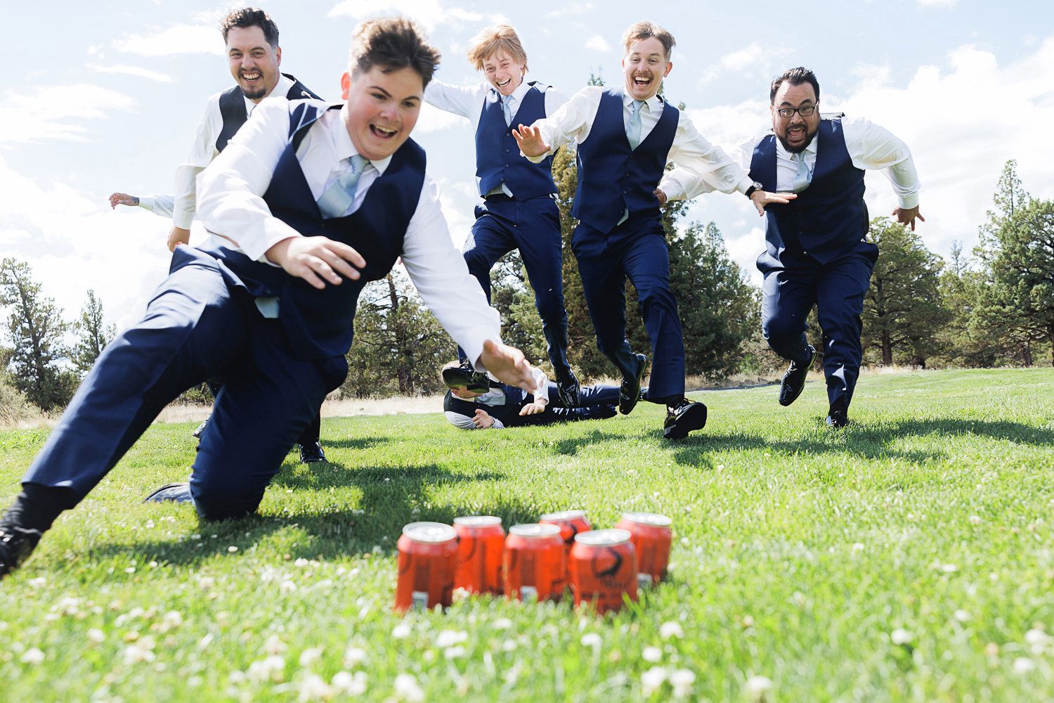 A group of people kneel in the grass while playing a team game with red cups on a sunny day outdoors.