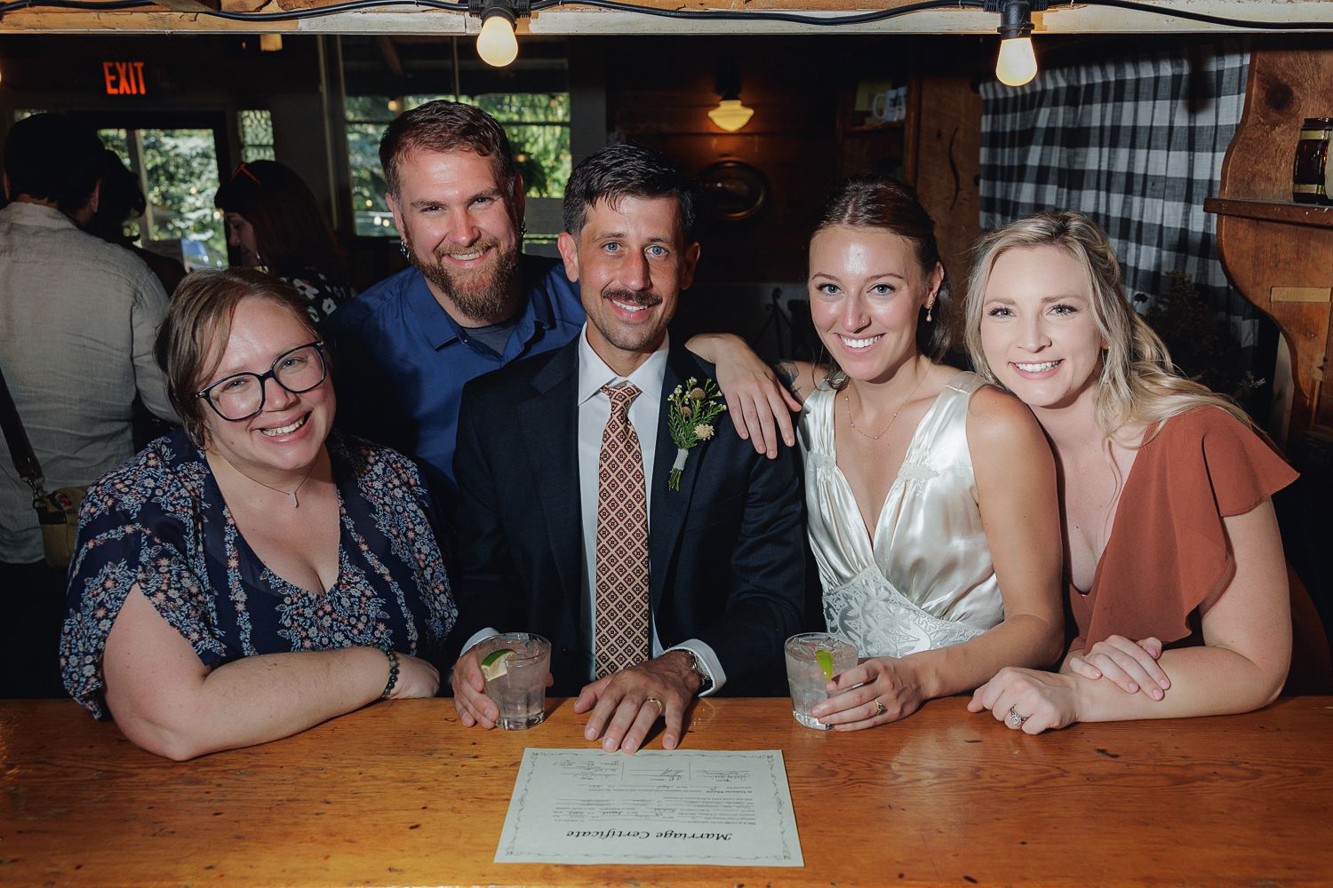Small group smiles together at a cozy restaurant bar with rustic wood decor and warm lighting.