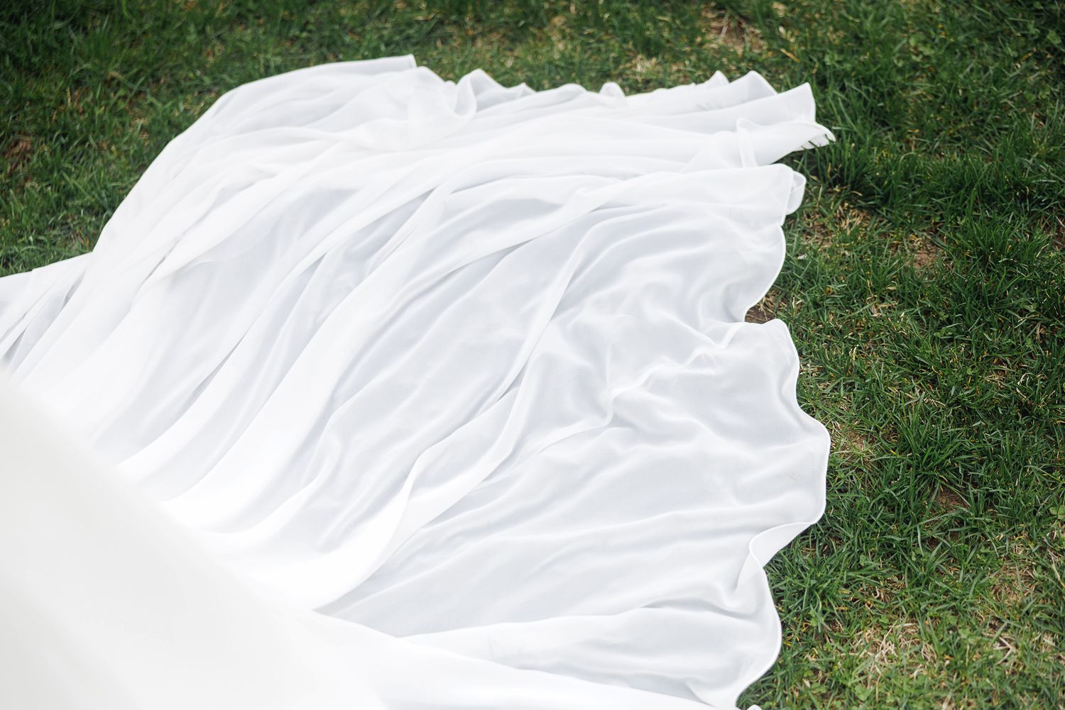 White fabric draped elegantly on green grass outdoors in natural light.