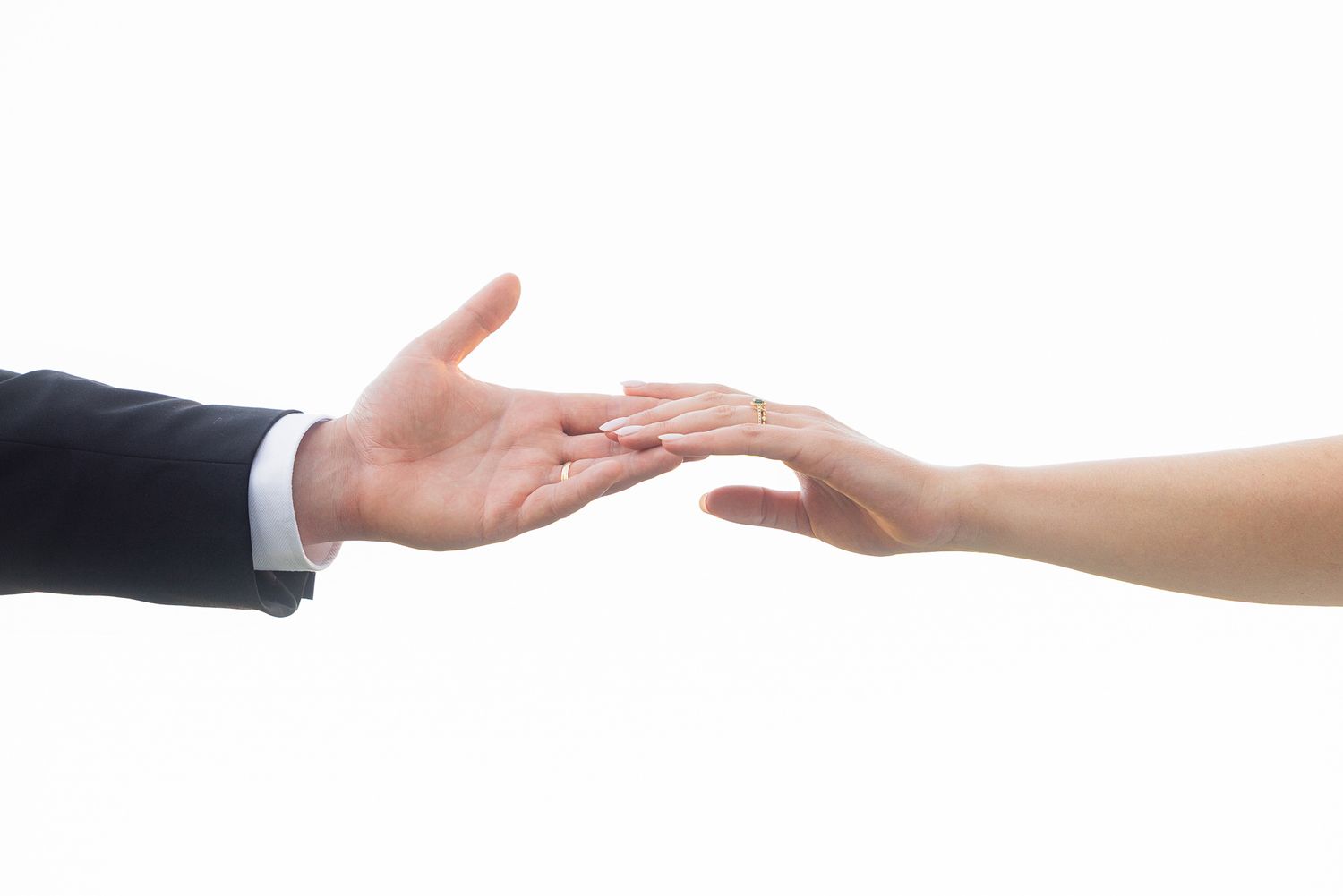 Close-up of a man in a suit and woman gently reaching toward each other's hands against a white background.