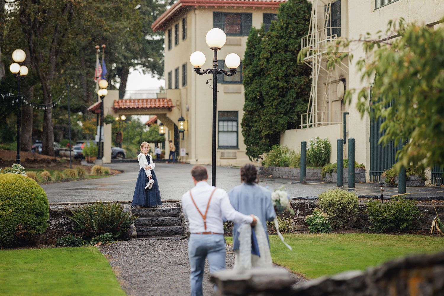 Students walking along a tree-lined path on a college campus with Spanish-style architecture in the background.