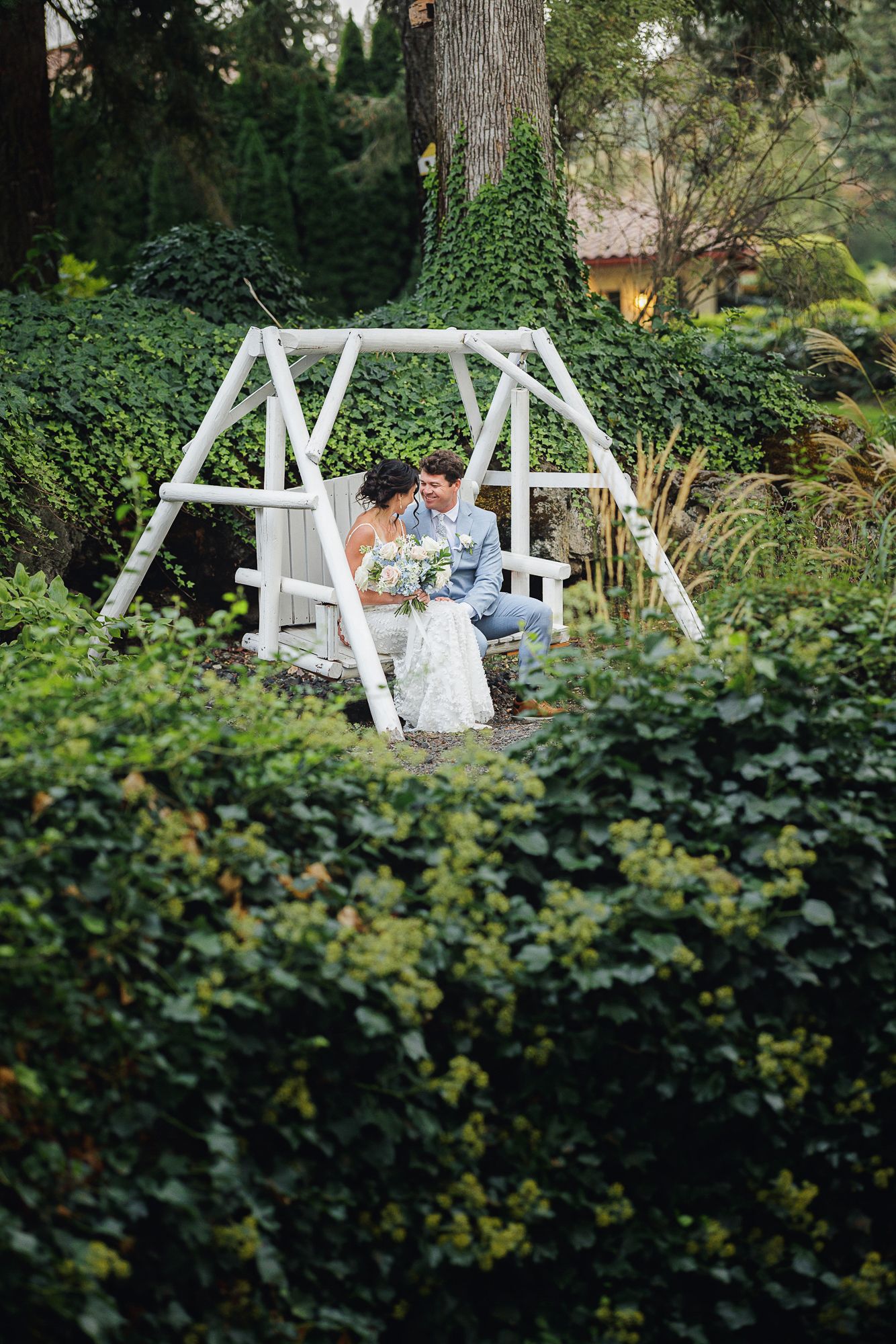 White garden swing set surrounded by lush greenery creates a peaceful outdoor seating area in a backyard garden.