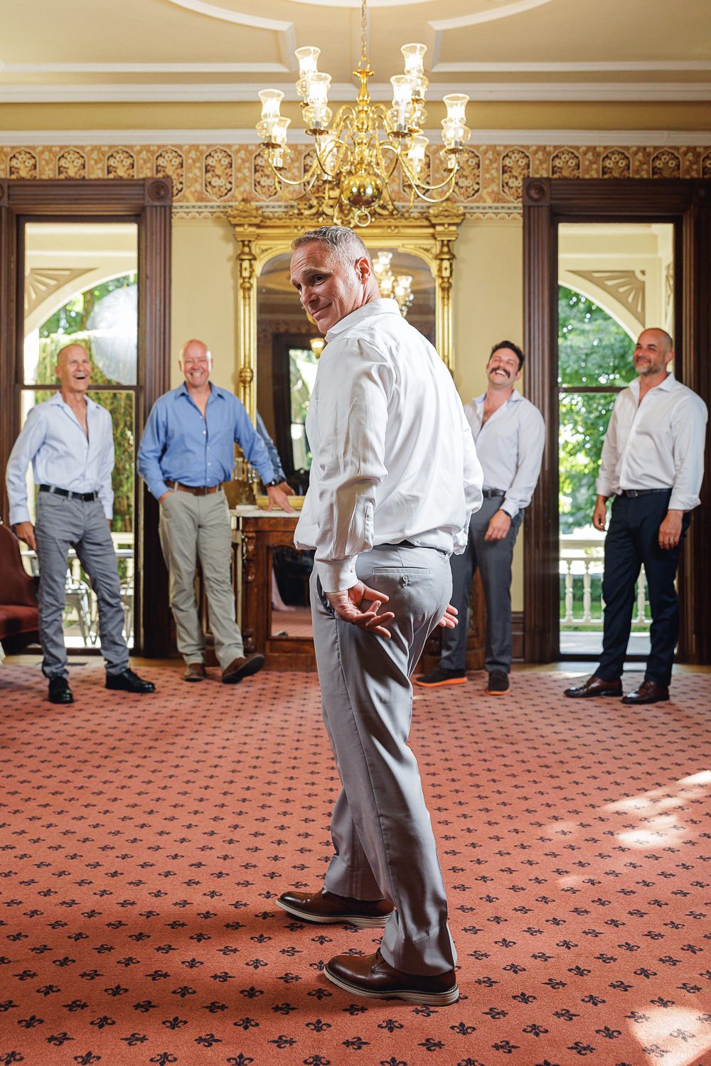 A group of seniors enjoy a ballroom dance lesson in an elegant room with chandeliers and patterned carpet.
