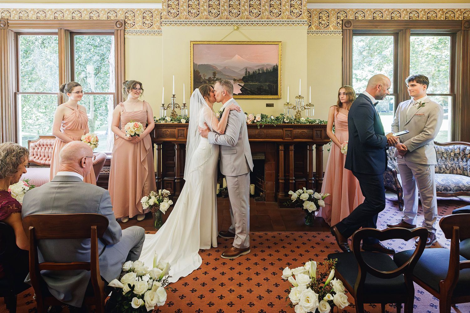 People stand in a church sanctuary during a wedding ceremony with ornate decor and floral arrangements.