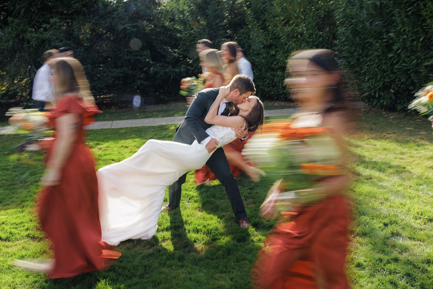 A group of people in orange robes walk through a sunny garden path in a blurred motion sequence.