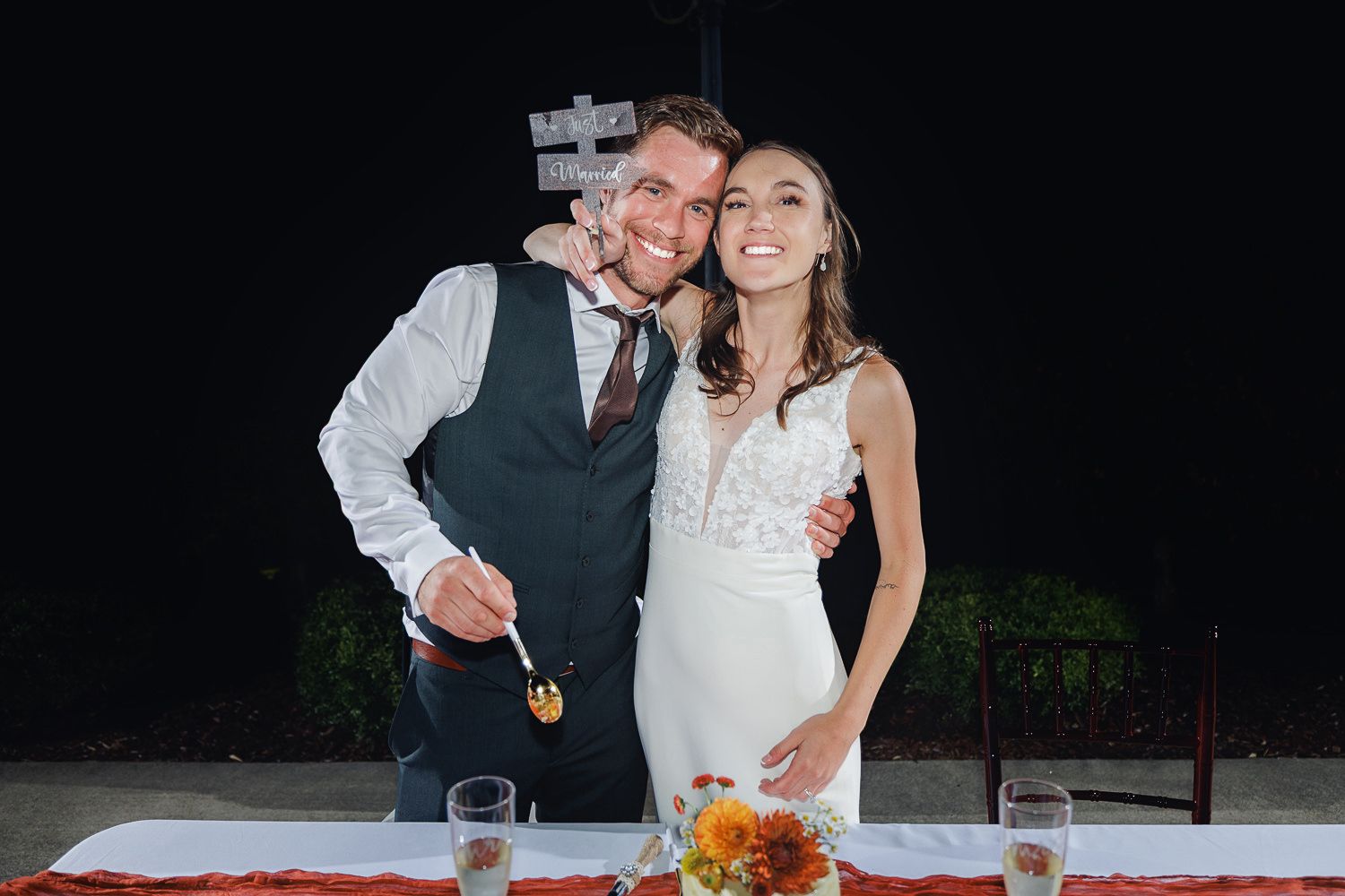 A joyful couple poses together at their wedding reception with drinks and floral centerpieces on the table.
