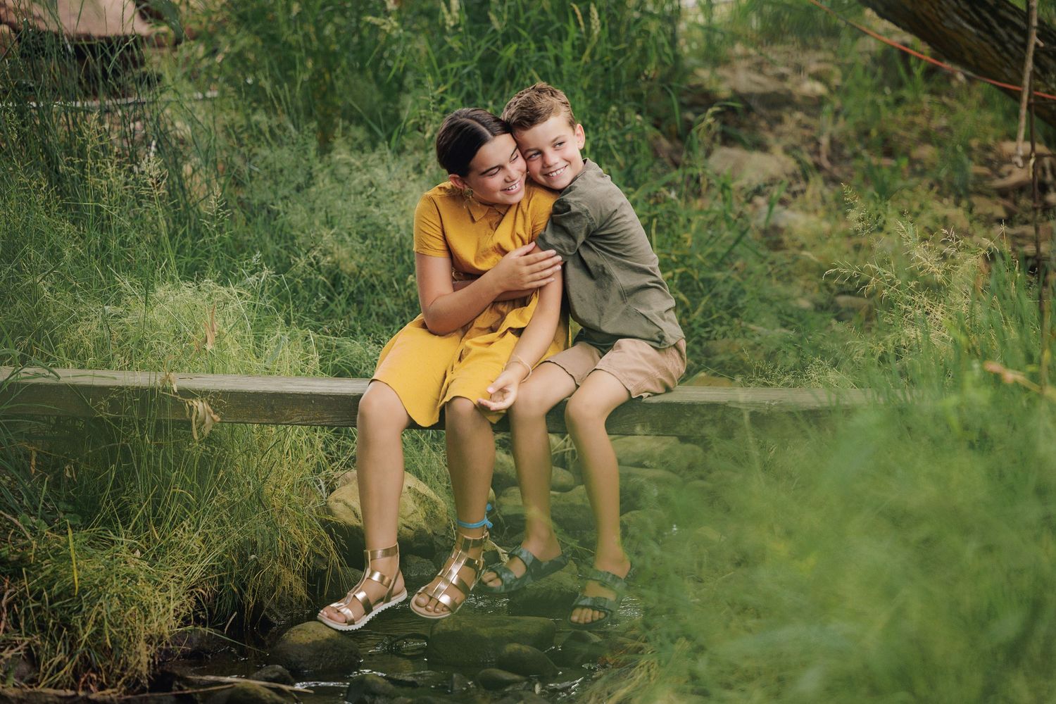 Two people sharing a tender moment while sitting on a wooden fence in a green meadow.