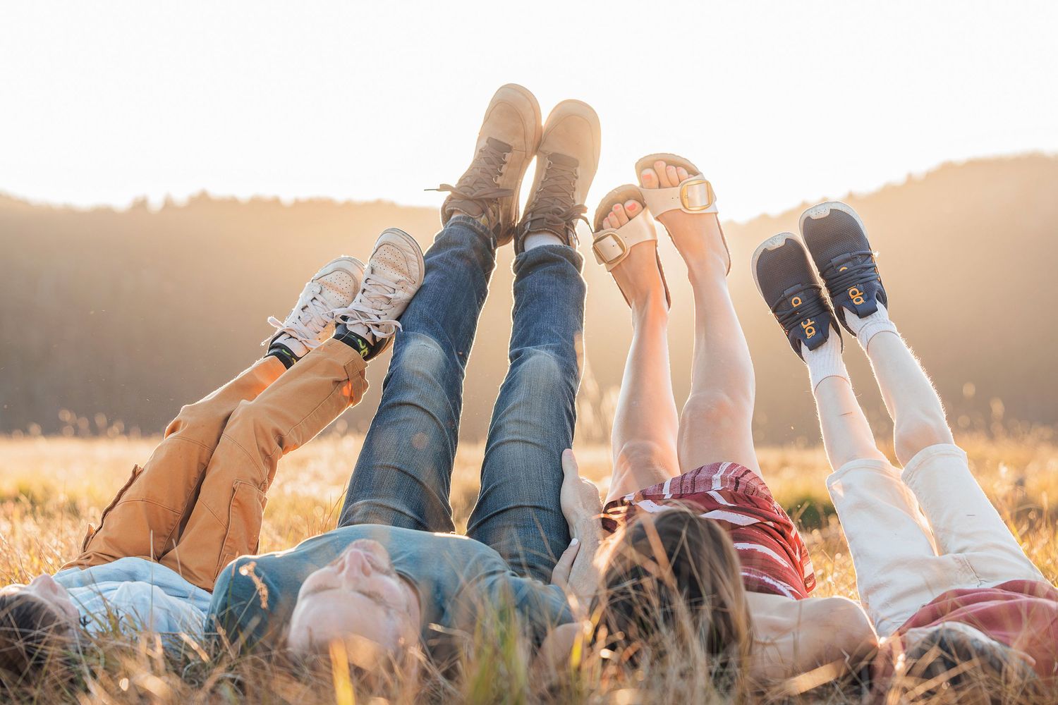 Group lying in grass raising their feet together at golden sunset.