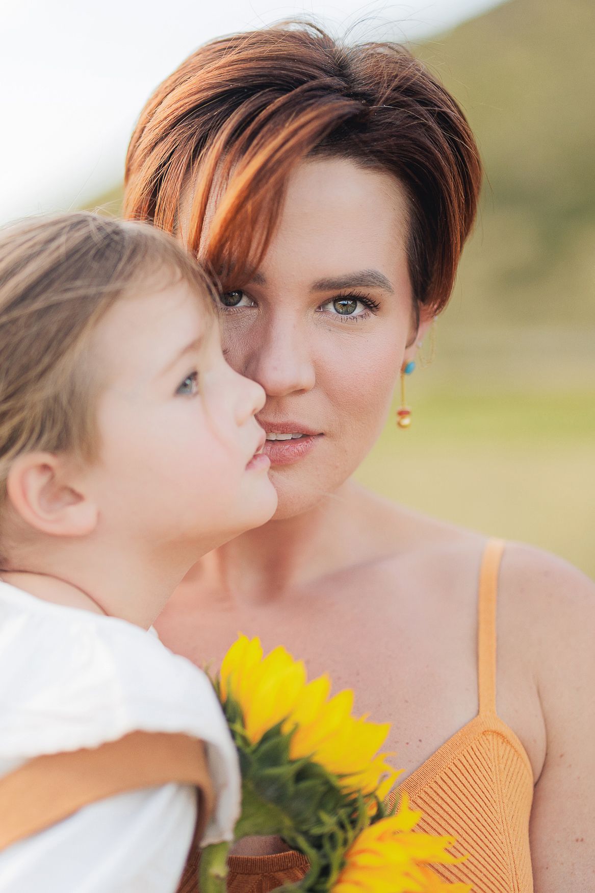 Mother and child share a tender moment with bright yellow sunflowers on a sunny summer day.