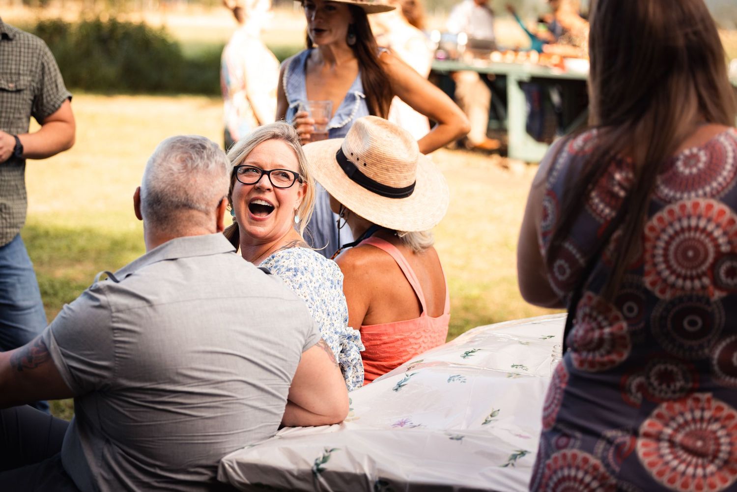 People enjoying conversation and laughter while seated at an outdoor gathering on a sunny afternoon.
