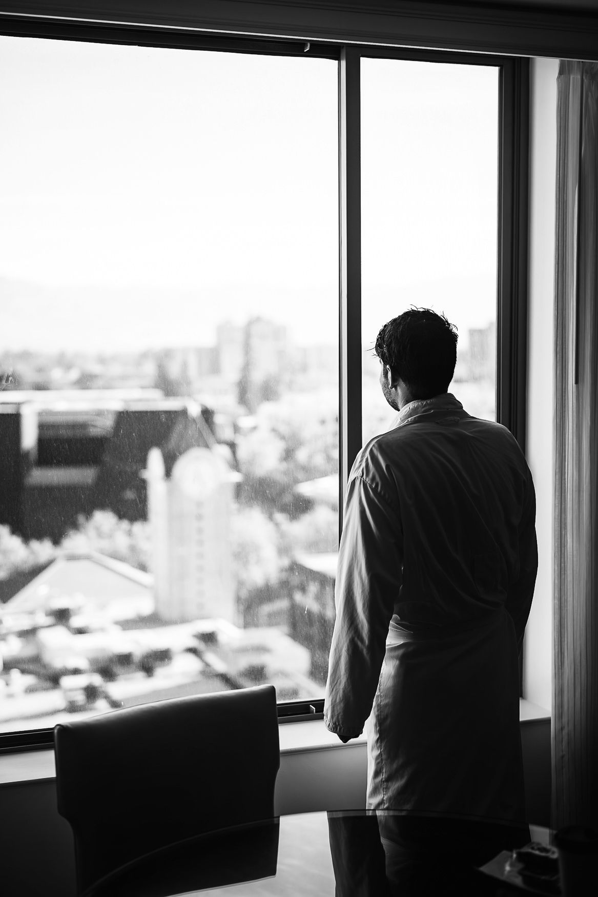 Black and white silhouette of someone in business attire gazing thoughtfully through large office window at city skyline view.