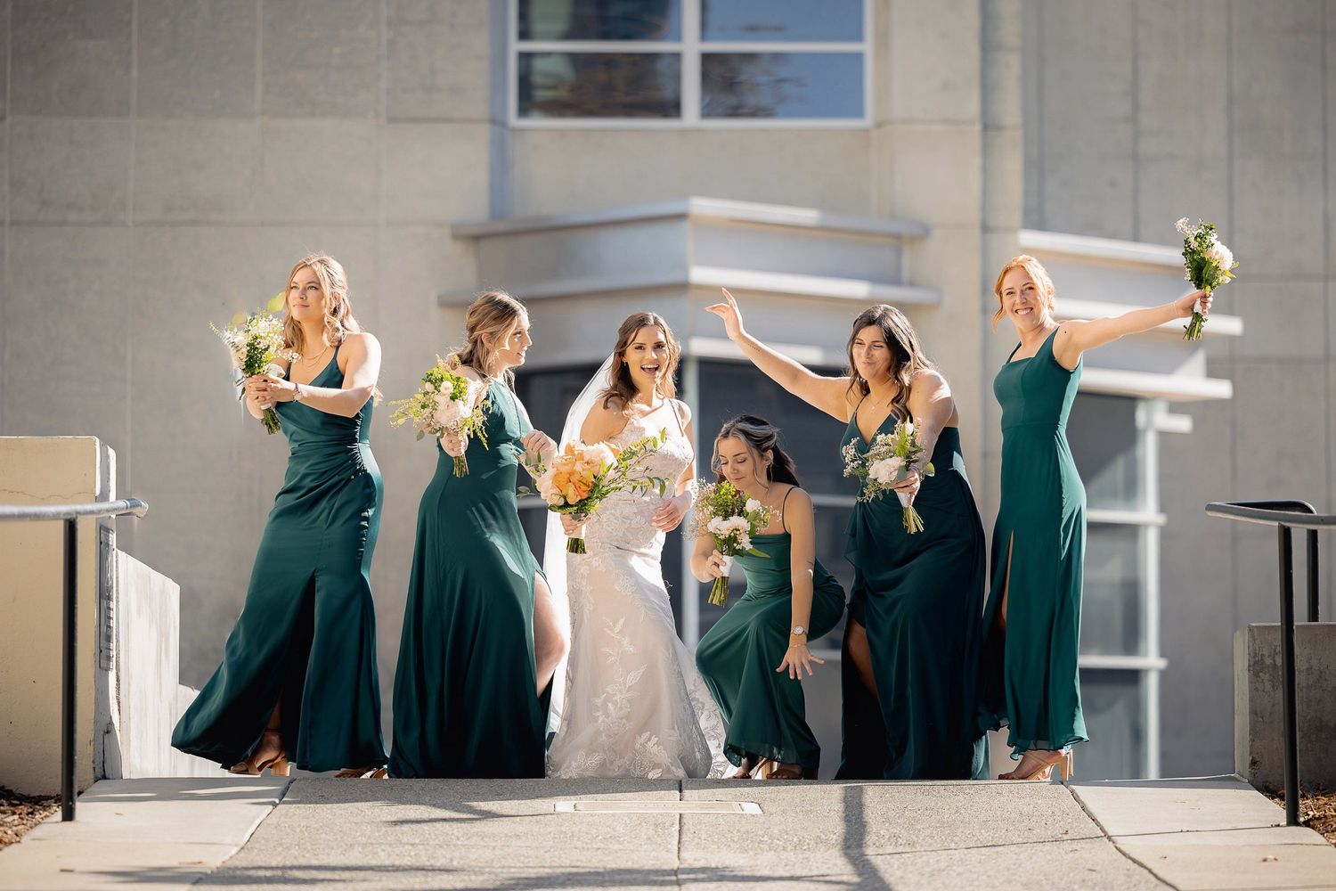 A bridal party wearing emerald green dresses dance and celebrate joyfully on an outdoor terrace.