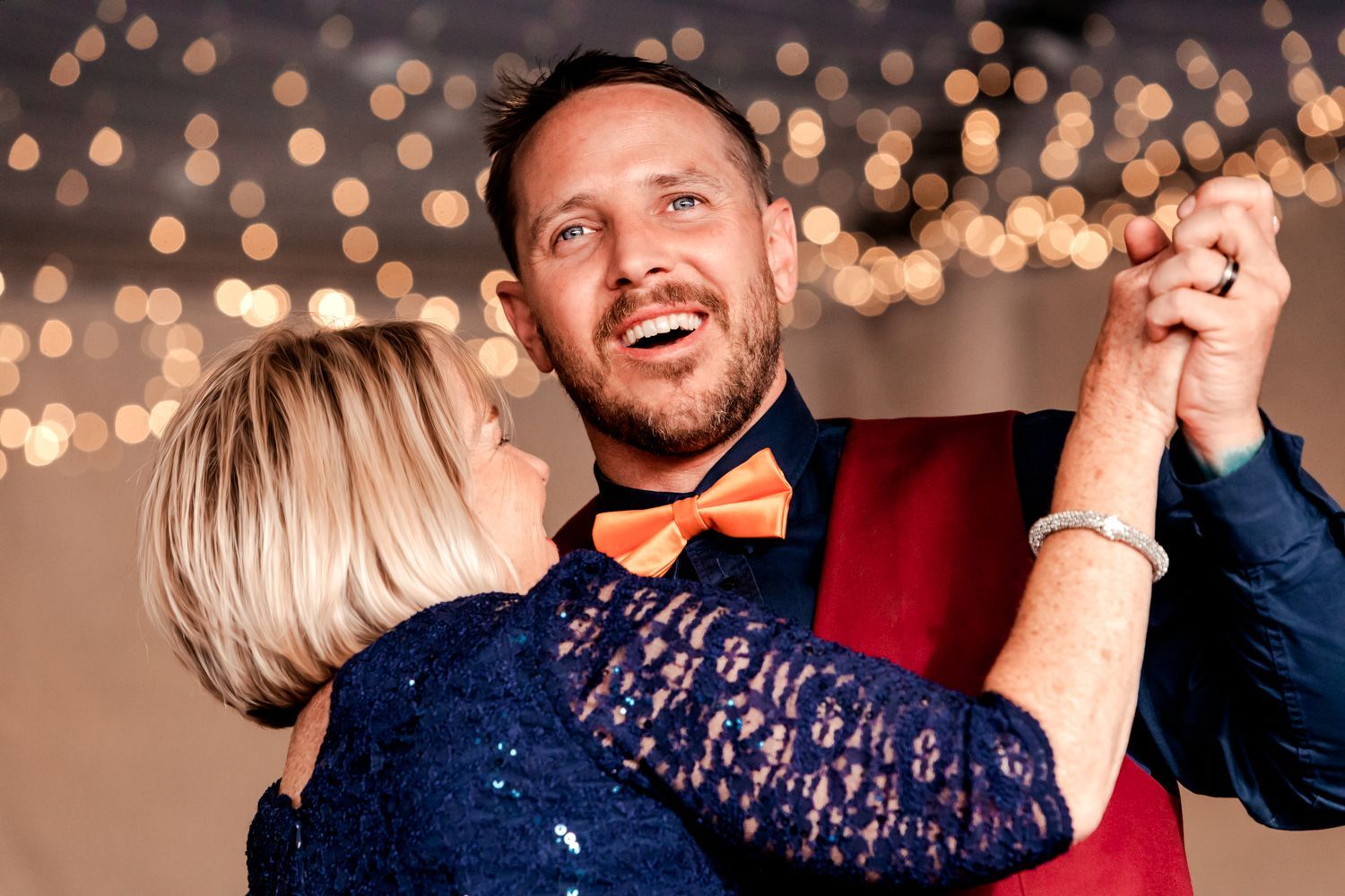Couple dancing together under romantic twinkle lights at an evening celebration with elegant formal attire.