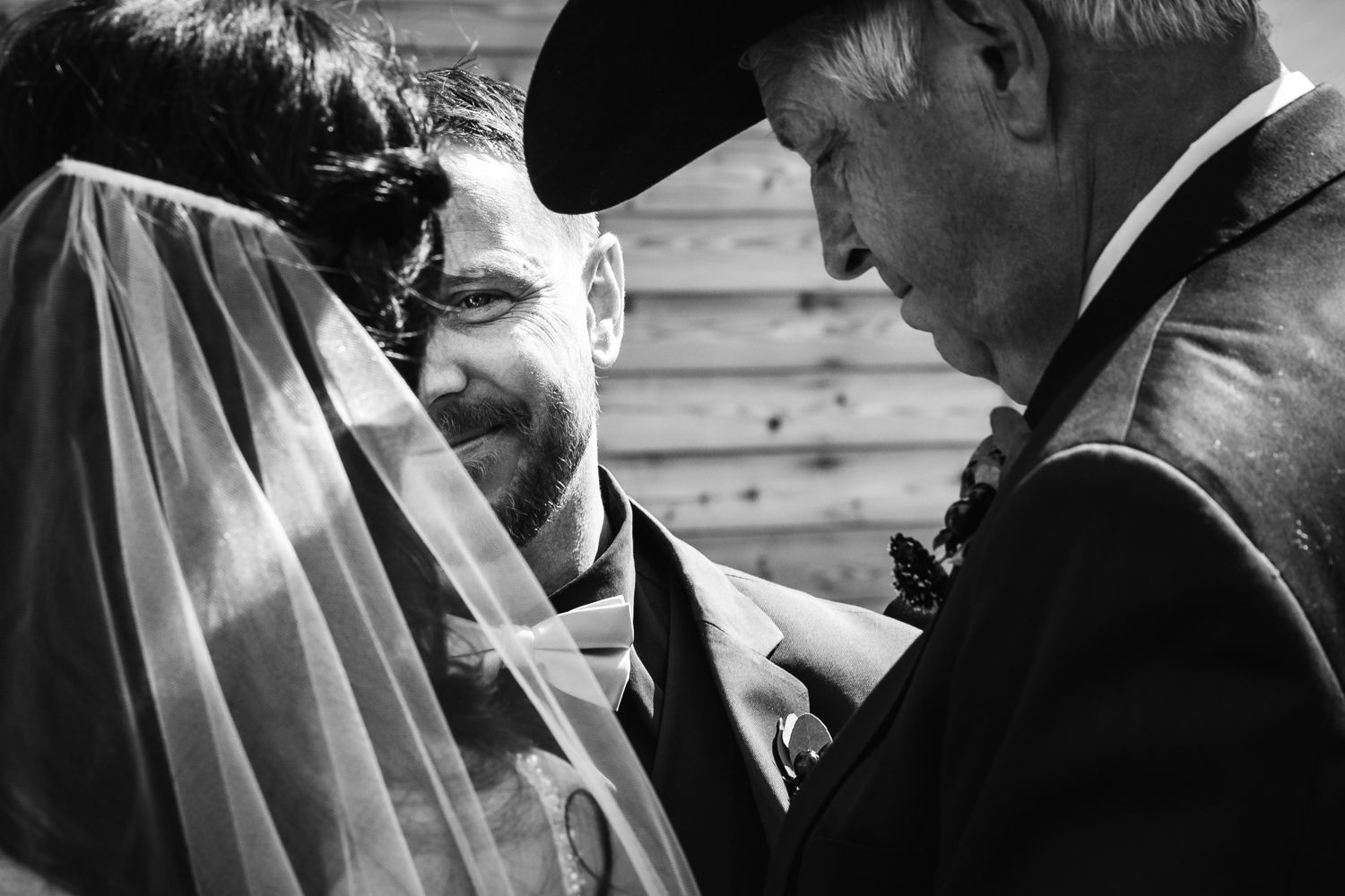 Intimate black and white moment between a bride in her veil and an older man wearing a cap at a wedding ceremony.