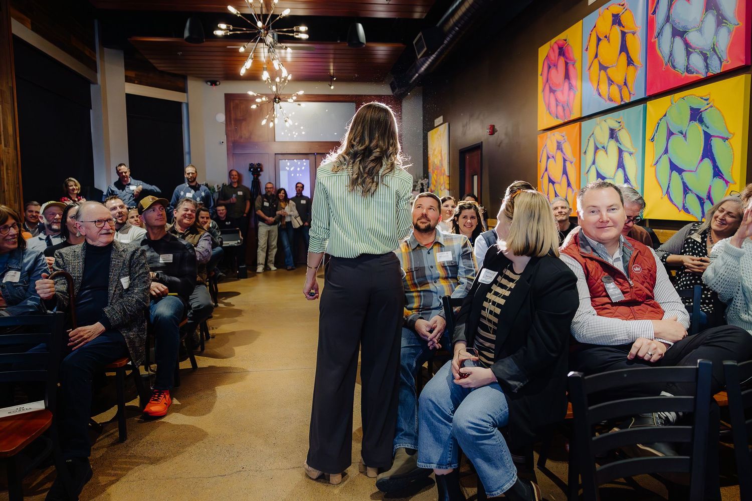 Speaker presenting to seated audience in venue with vibrant wall art and industrial ceiling.