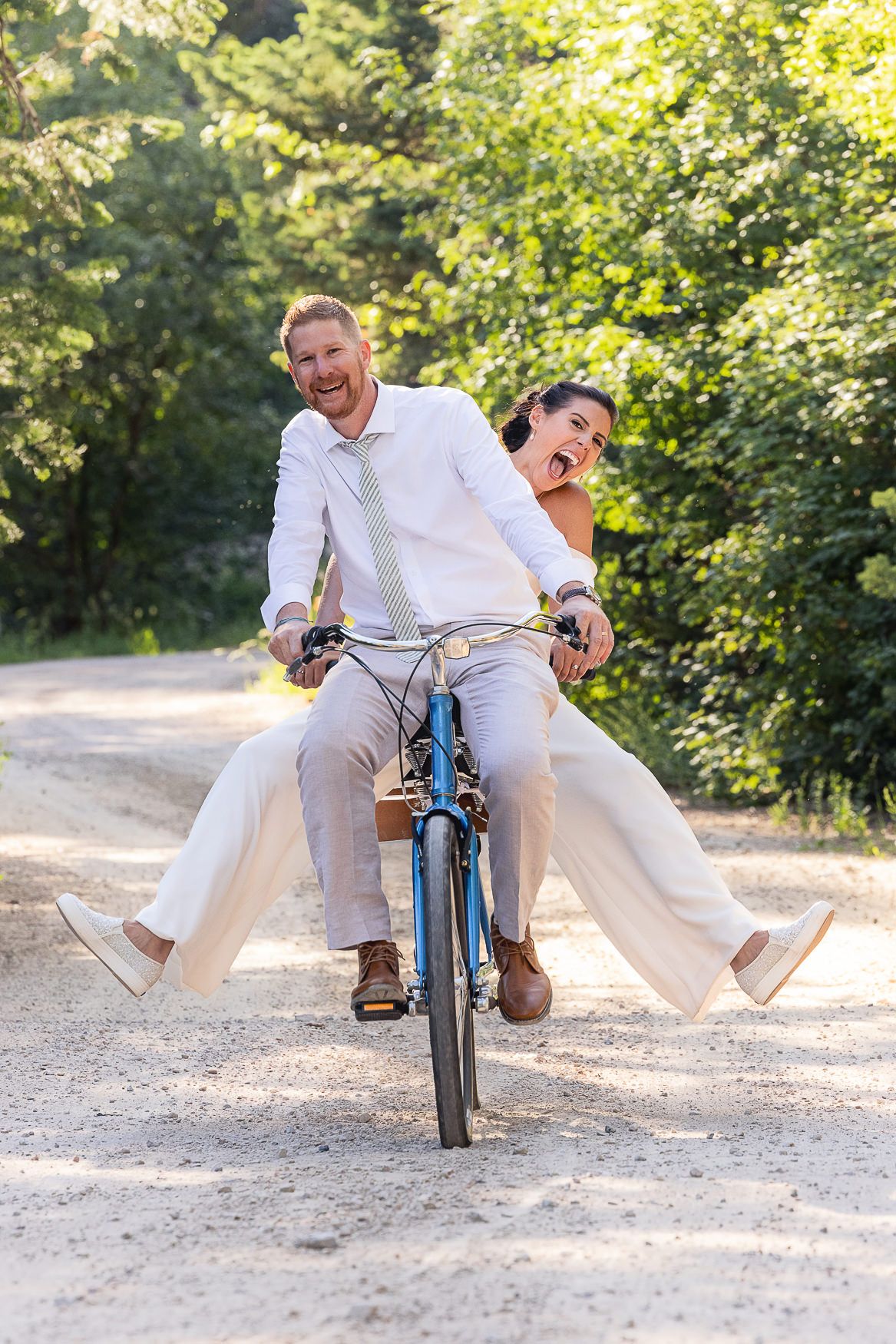 A playful couple rides together on a blue bicycle on a sunny forest path.