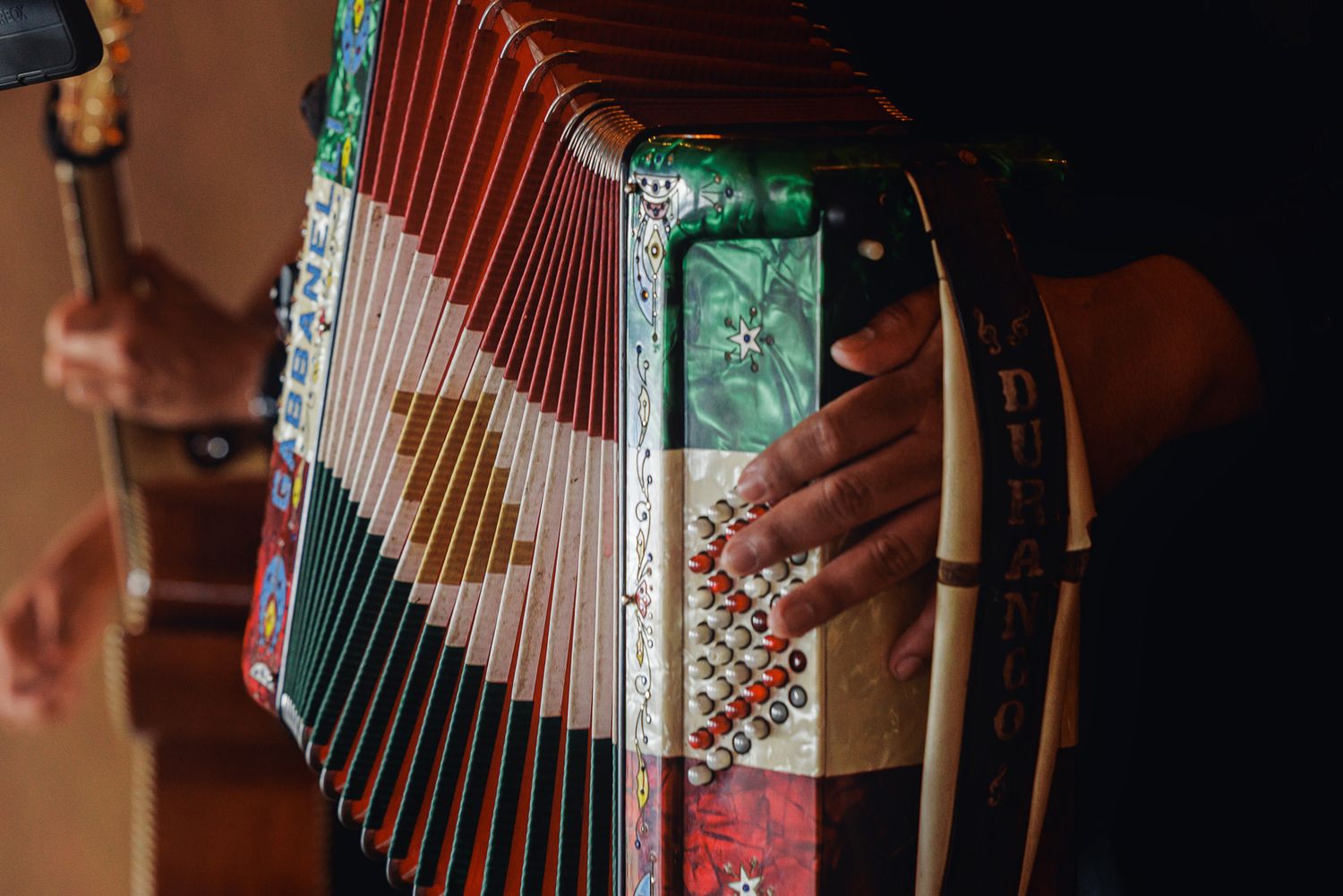 Close-up of hands playing a colorful decorative accordion with red and green pearl finish and white keys.
