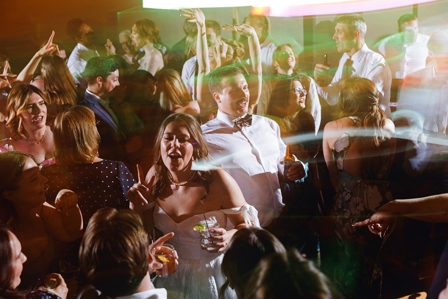 Couple dancing joyfully at a lively wedding reception party with guests celebrating on the dance floor.