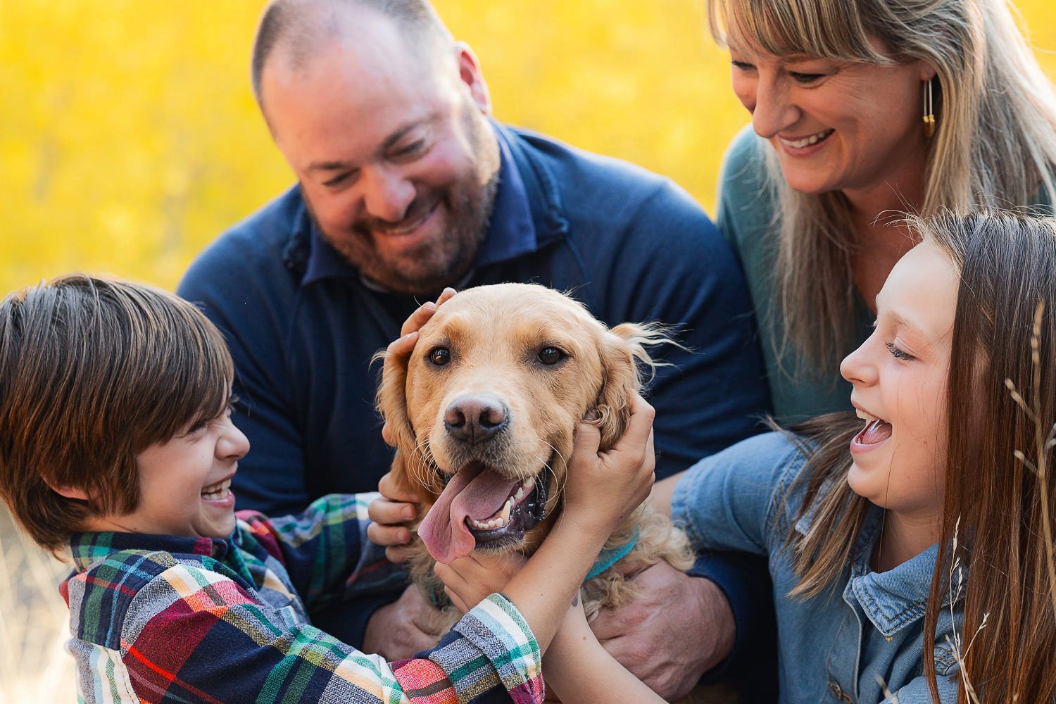 A playful golden retriever puppy interacts with a family while taking photos during an outdoor portrait session.