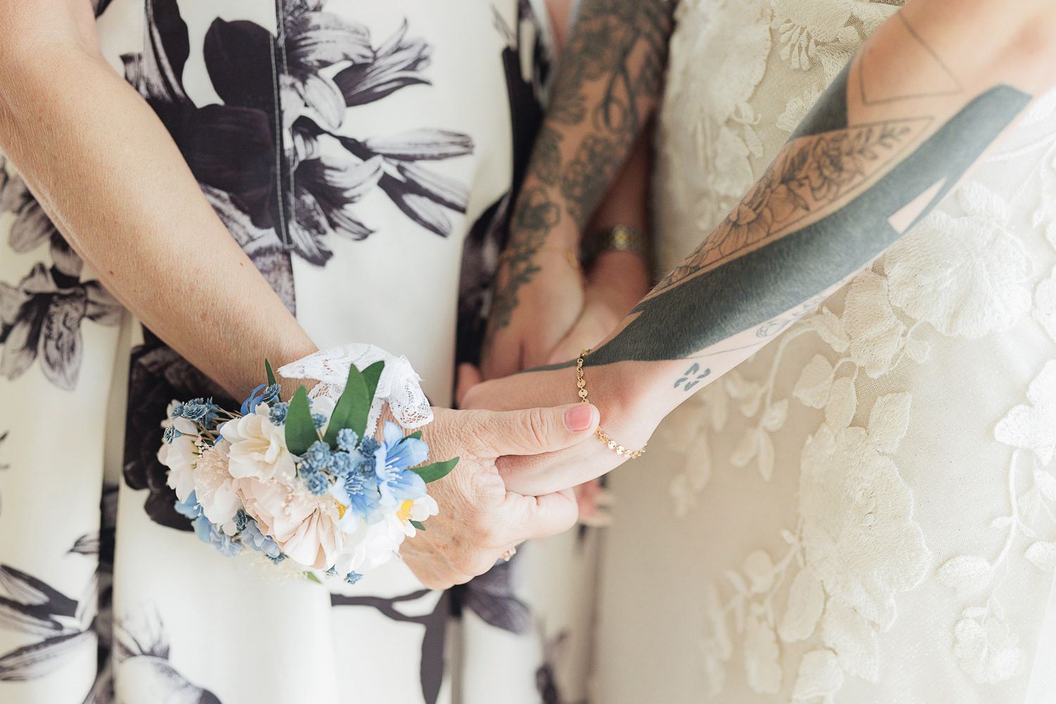 Close up of hands holding decorative flowers against floral patterned fabric at a wedding ceremony.