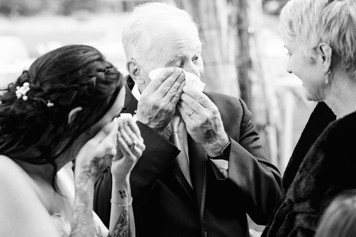 Black and white photo showing an emotional moment with tears at a wedding as people share a touching interaction.