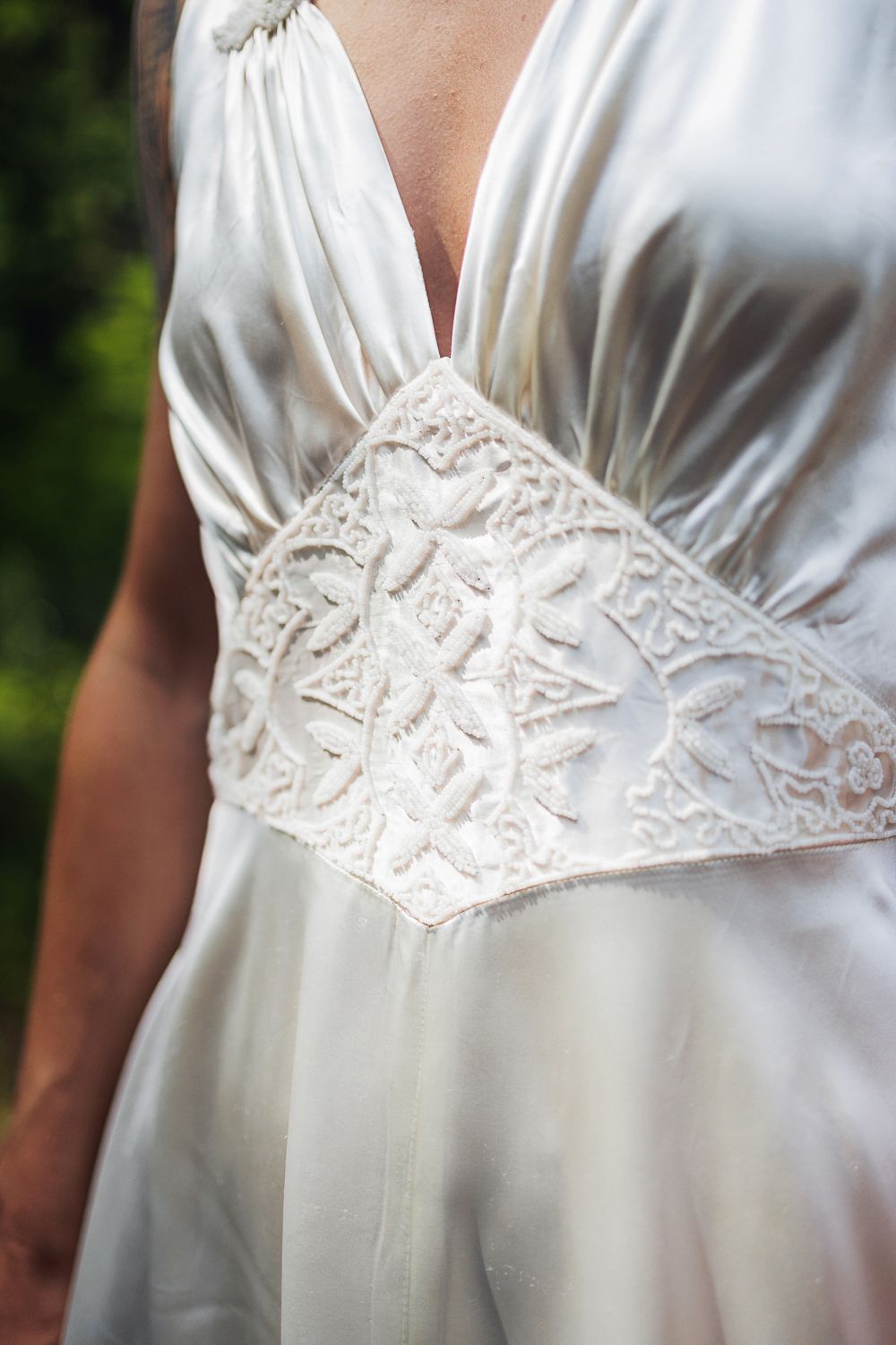 Close-up detail of white vintage wedding dress with delicate lace pattern and gathered fabric at empire waistline.