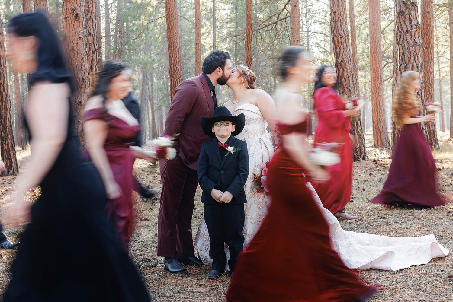 Blurred motion of people dancing in a circle among tall redwood trees in a forest setting.