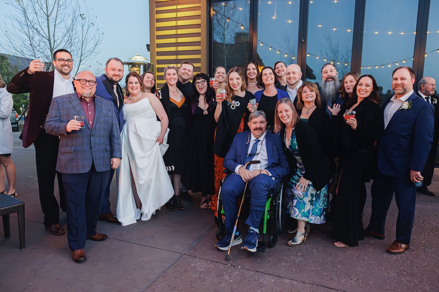 Wedding guests line up along a wall in formal attire for a group photo at an indoor venue.