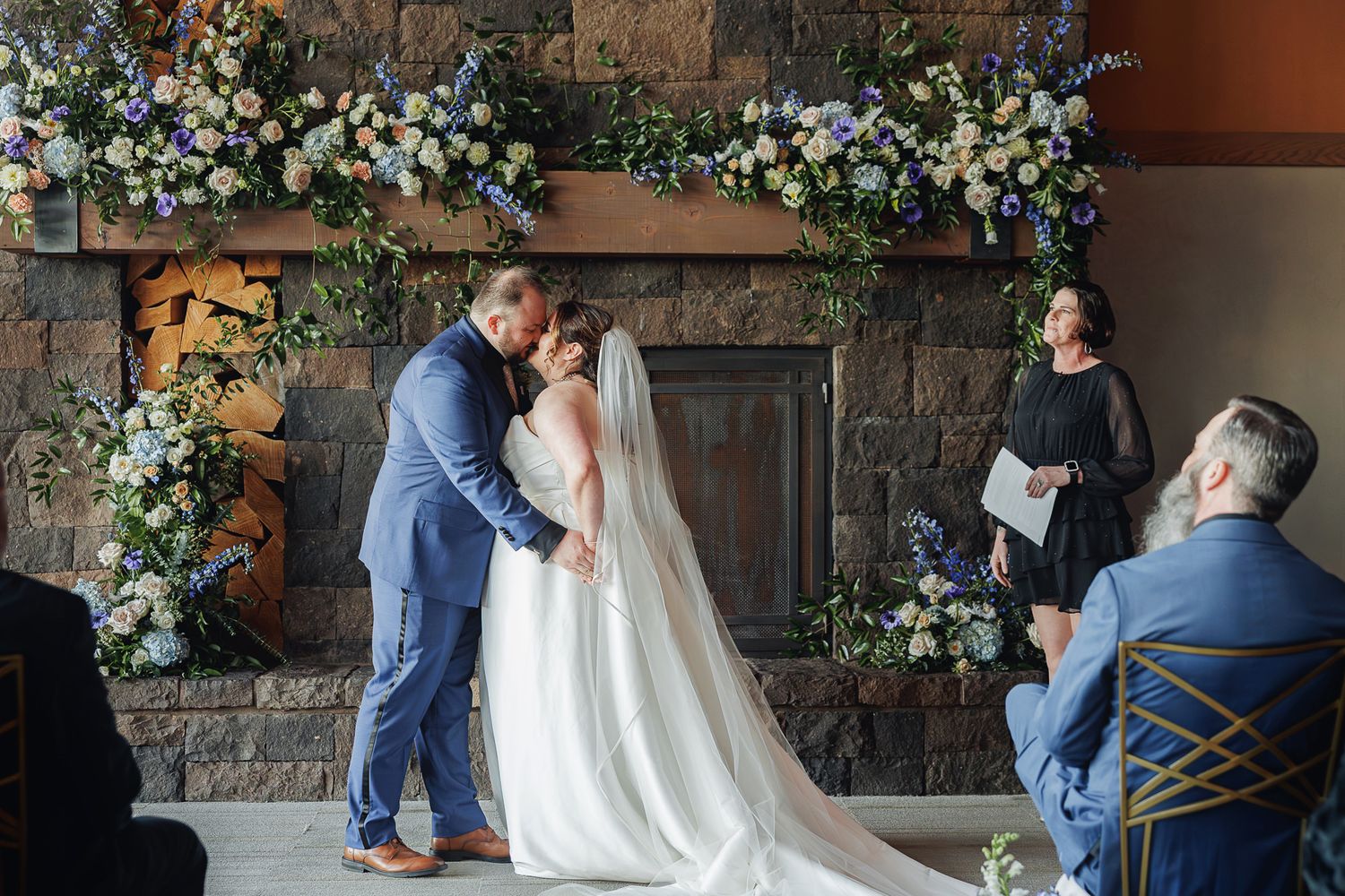A couple shares a romantic moment during their wedding ceremony against a stone wall backdrop with white floral decorations.
