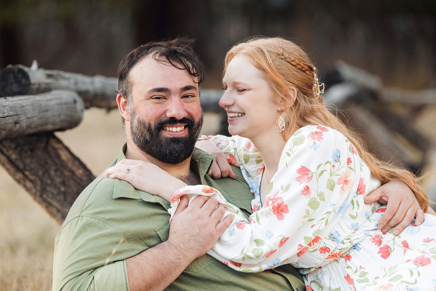 Happy couple embracing and smiling together outdoors near rustic wooden fence.