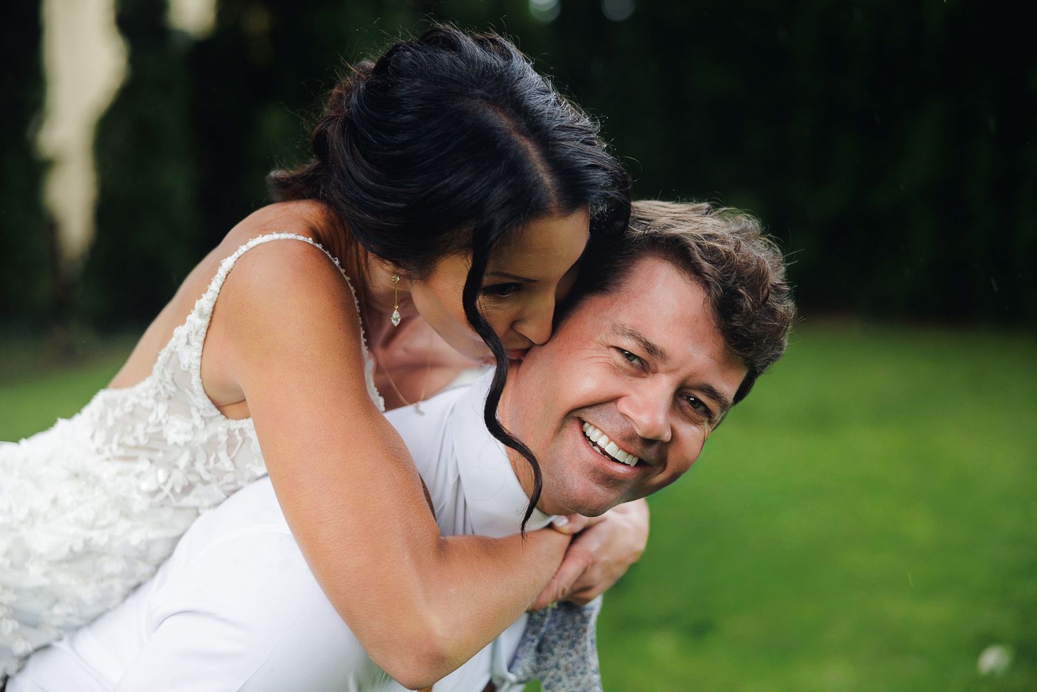 A joyful couple embraces and laughs together outdoors on a sunny day in a garden setting.