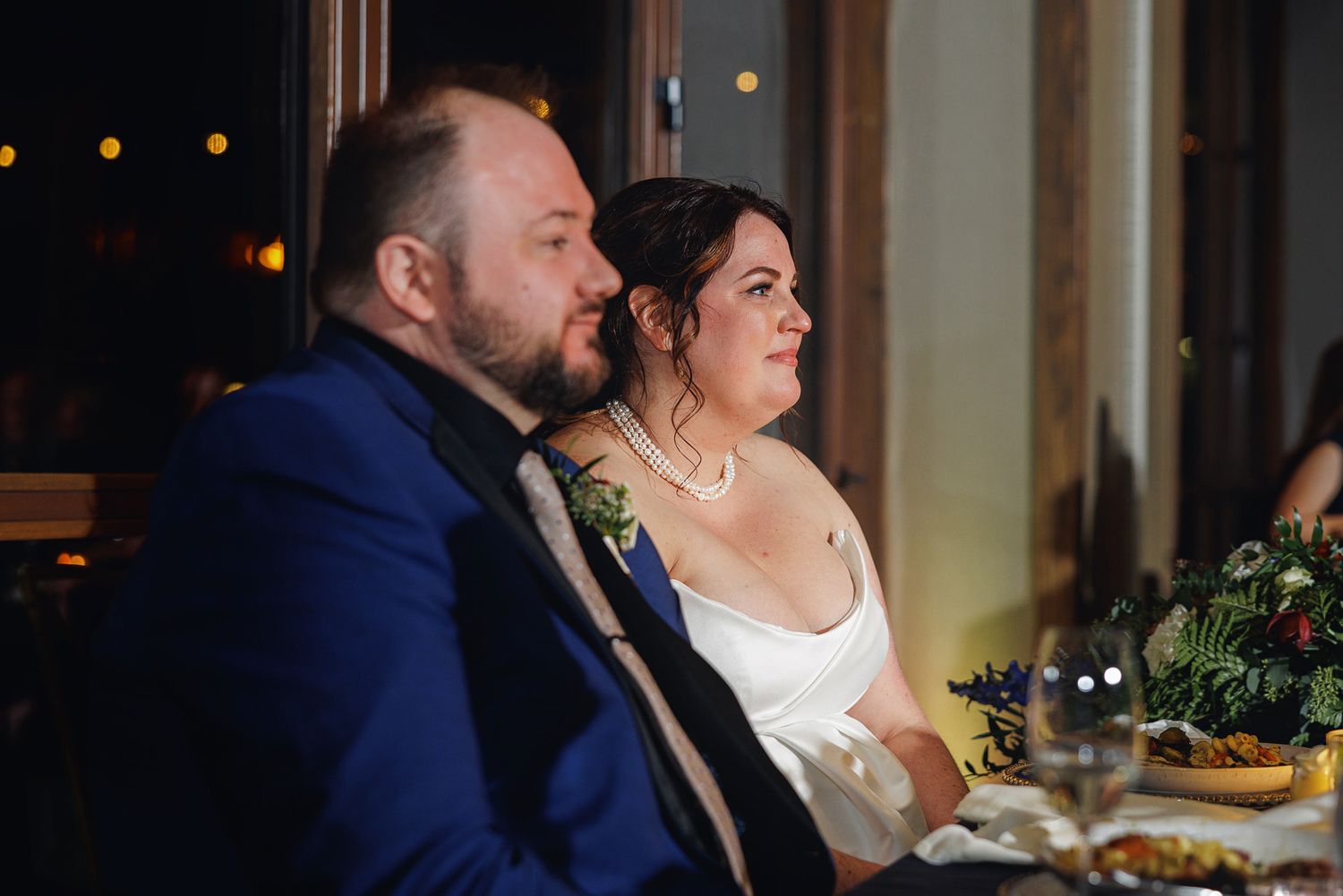 Wedding couple shares a tender moment during their reception while seated at a candlelit table.