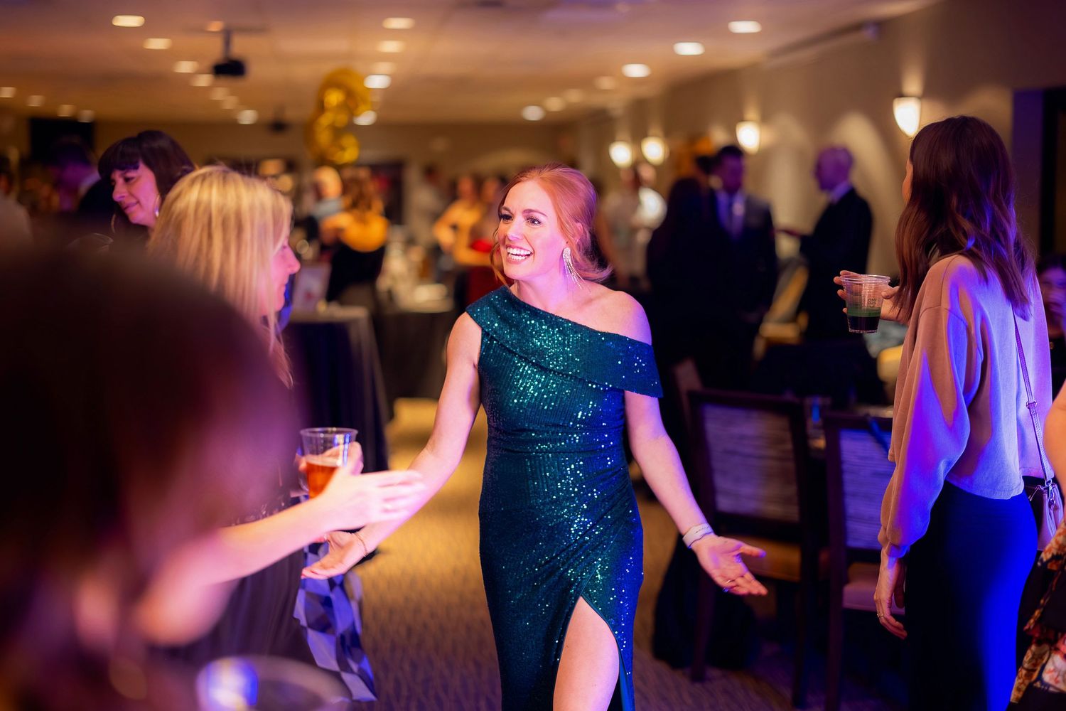 Woman in sparkly teal evening gown dancing at an elegant party venue with ambient lighting.