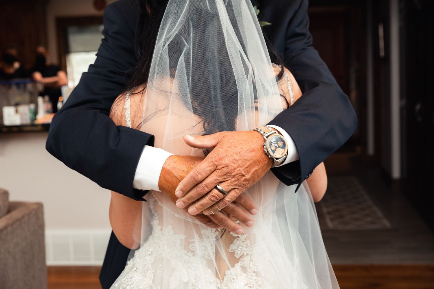A close-up detail of hands wearing a luxury watch and holding delicate white bridal veil fabric.