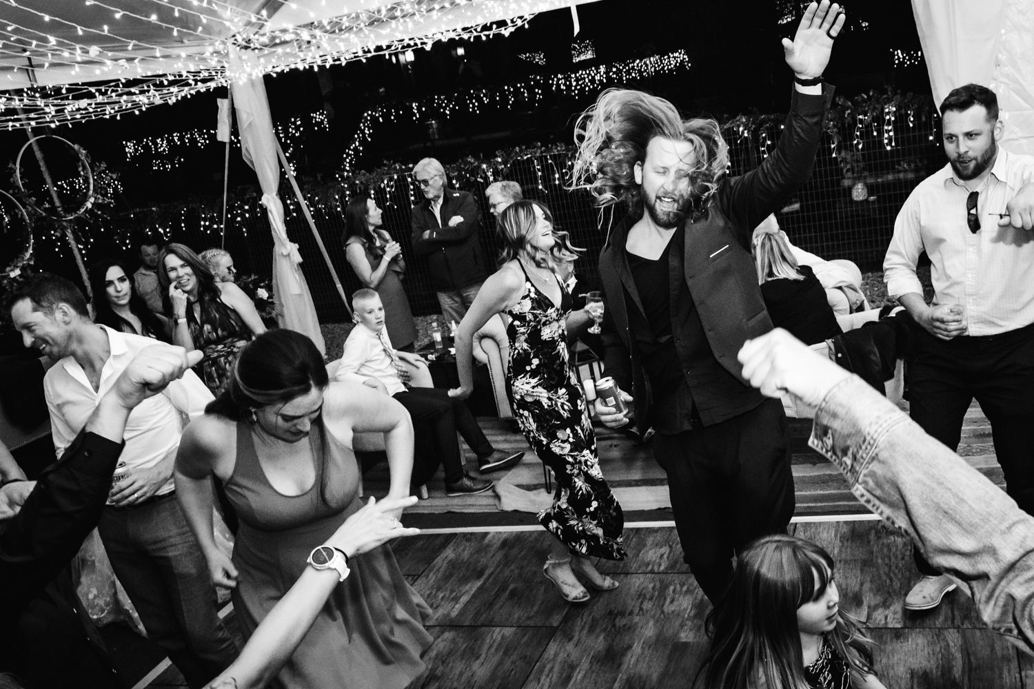 People dancing energetically in a black and white photograph at what appears to be a lively party or club event on a dance floor.