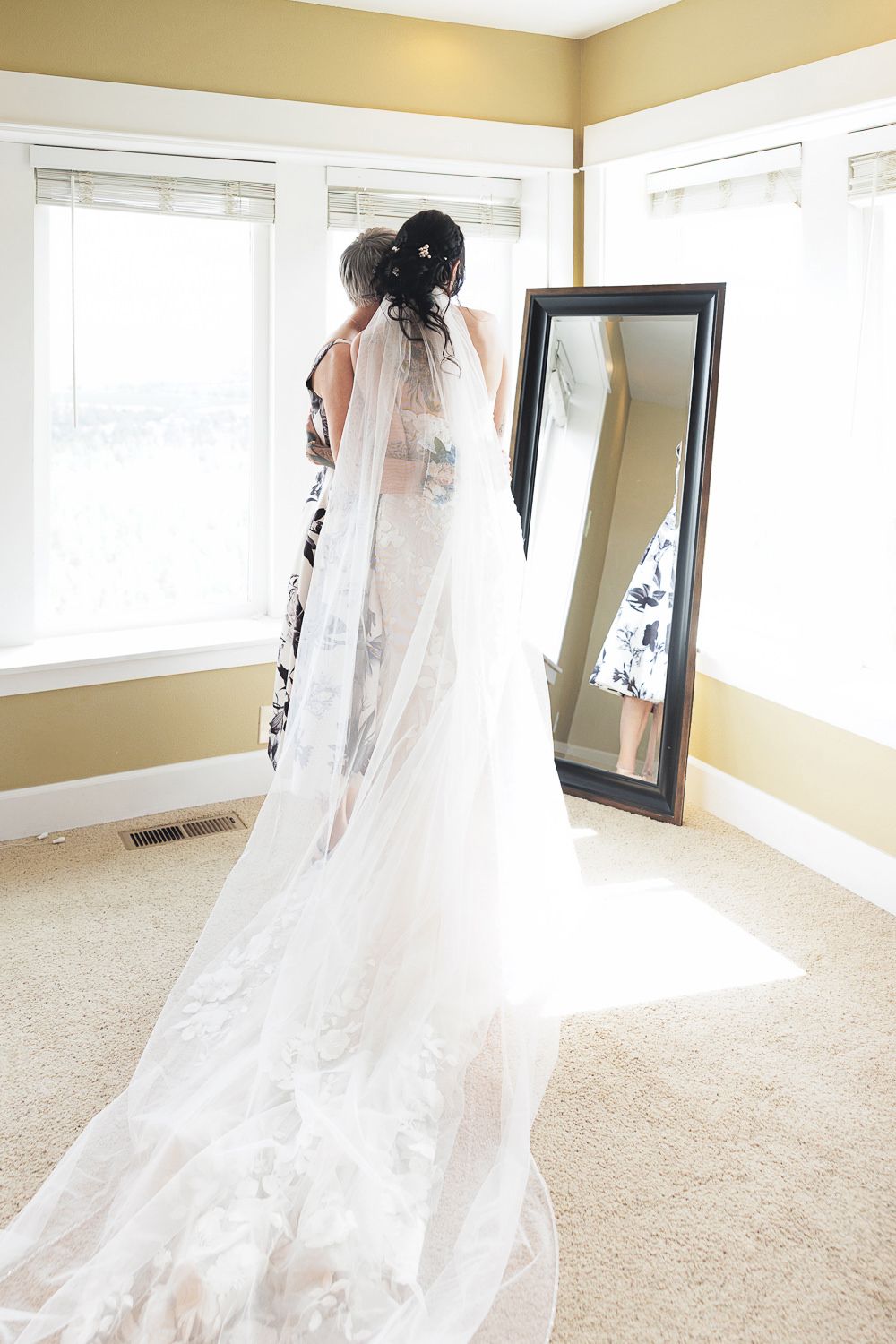 A bridal figure in a flowing white wedding dress and long veil stands gracefully in a sunlit room.