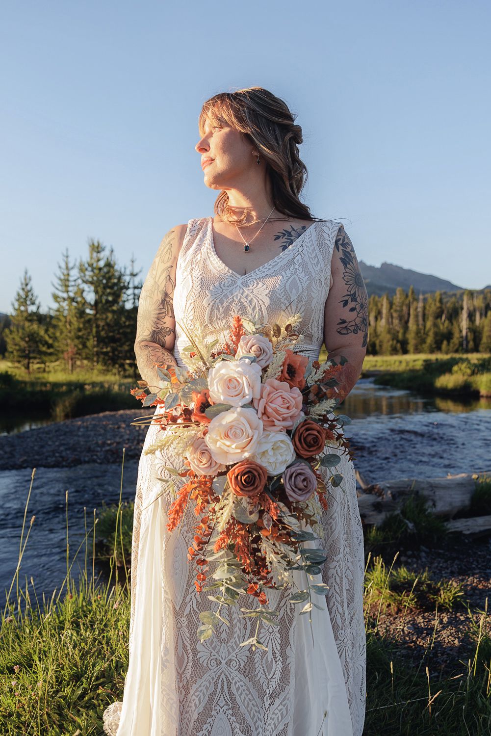 Beautiful bridal bouquet with pink and peach roses against a sunset mountain landscape in a wedding dress with lace detail.