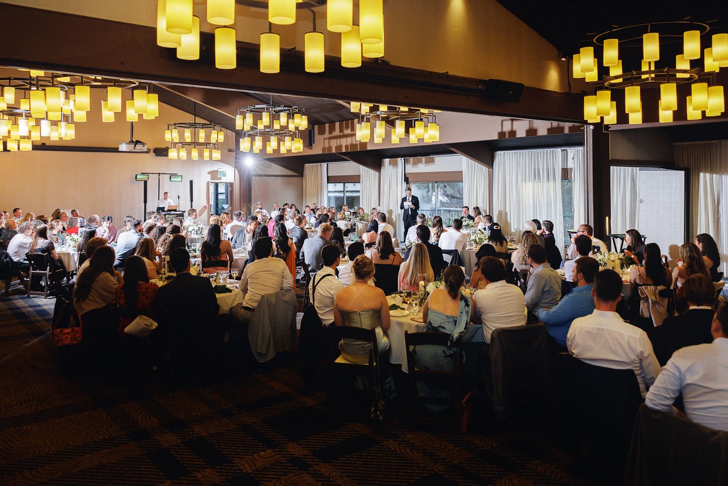 Elegant banquet hall filled with guests dining under warm pendant lights at a formal event.