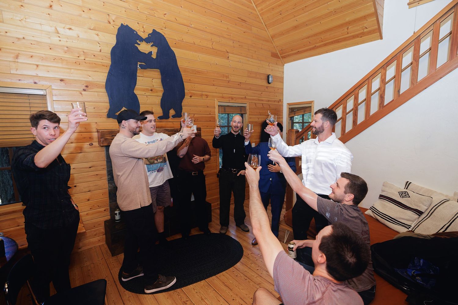 Group of people raising glasses in a toast inside a rustic wood-paneled cabin with a bear decoration on the wall.