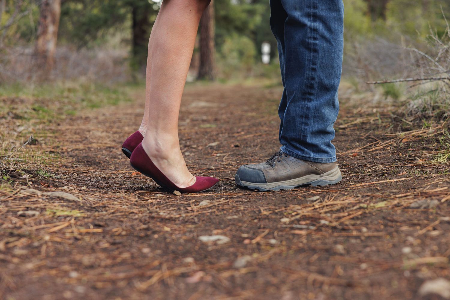 Close-up of a couple standing face to face on a forest path, wearing red flats and hiking shoes.