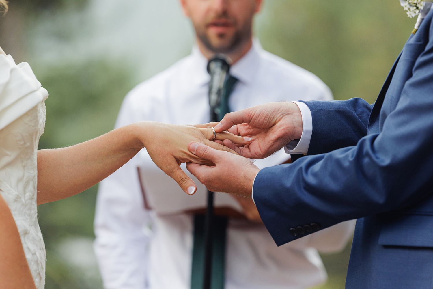 Close-up shot of hands exchanging wedding rings during an outdoor ceremony.