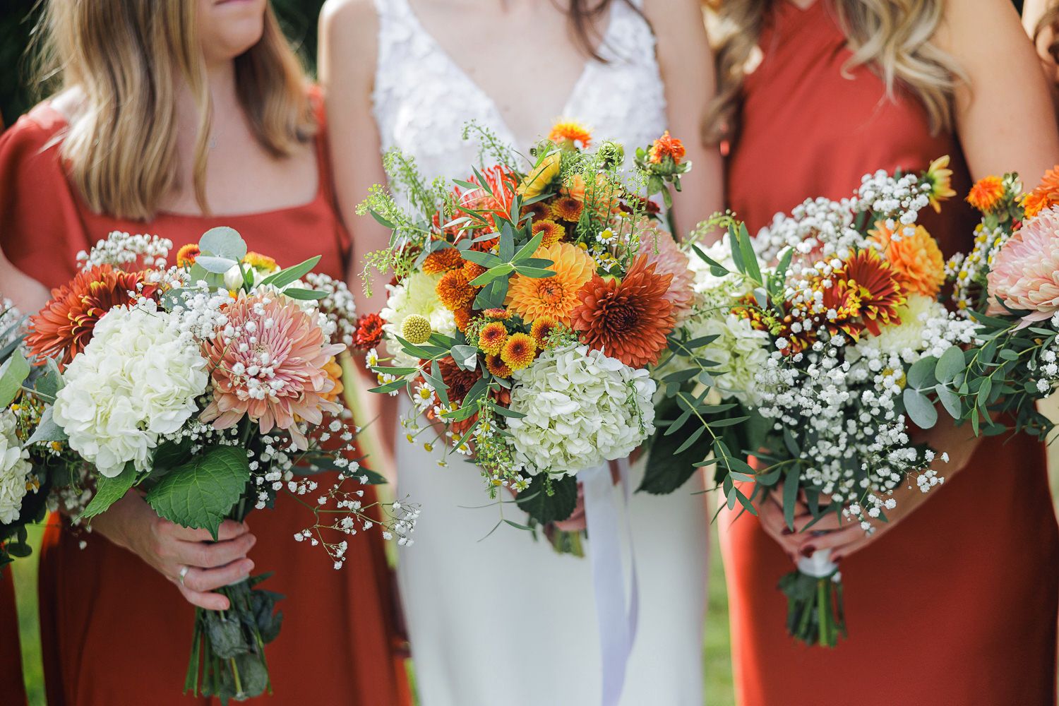 A row of coral-colored bridesmaids holding vibrant bouquets with orange, white and yellow flowers and greenery.