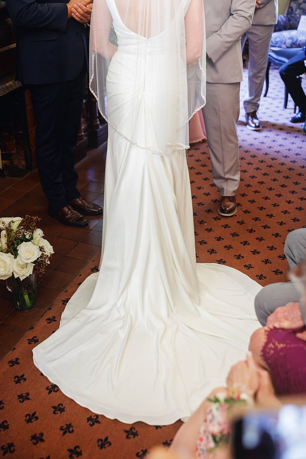 A flowing white wedding dress train on a patterned carpet floor during a ceremony.