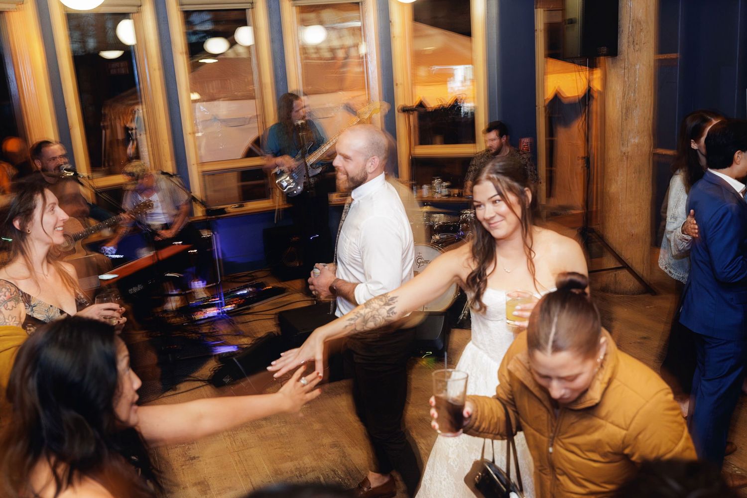 Bride and groom dancing joyfully with wedding guests at lively indoor reception party.