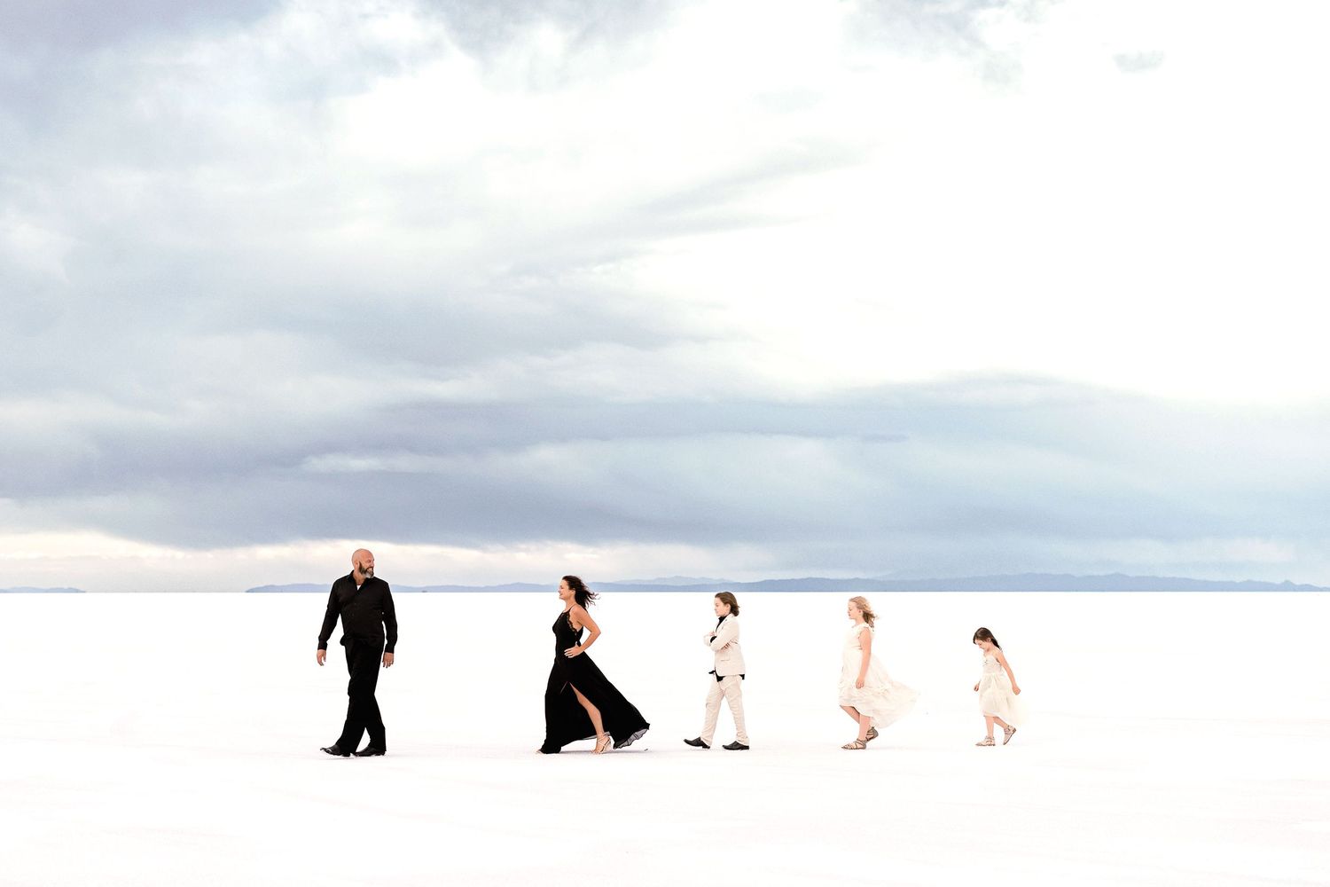 Five silhouettes walking in line across white landscape under stormy sky.