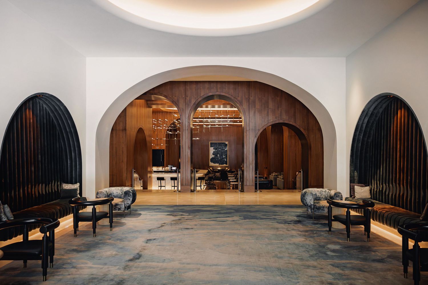Elegant hotel lobby with arched entrance, dark wooden benches, and warm lighting leading to a reception area.
