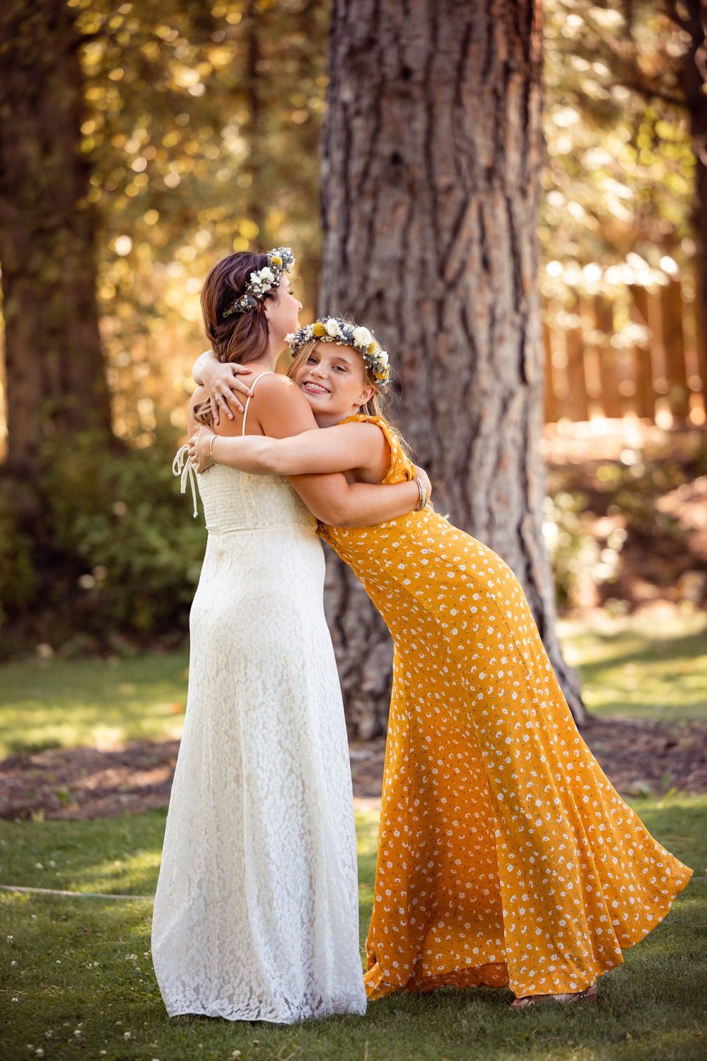 Two people embracing outdoors wearing a white lace gown and yellow polka dot dress at a sunny garden celebration.